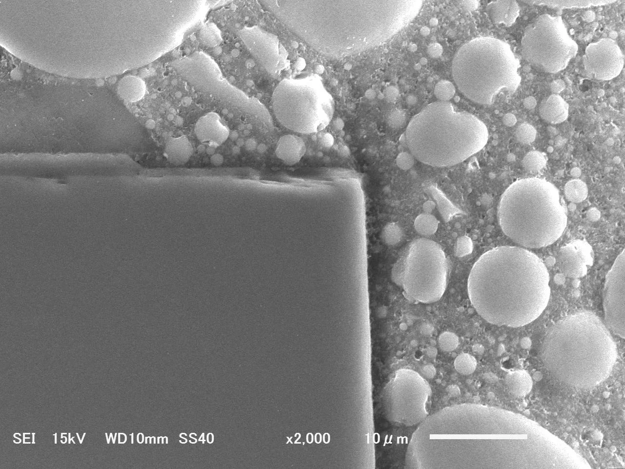 手研磨で断面出ししたSiCチップのSEM画像。エッジの欠けと研磨傷が見られる(×2,000)